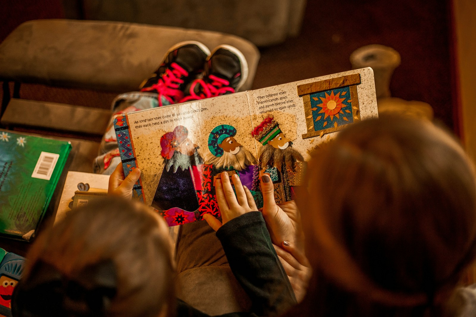 A child's hands rest on an open picture book, with warm home lighting and colorful illustrations on the pages.